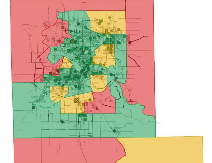 A map of Cedar Rapids census tracts shaded green, yellow and red, with dark lines along some roads, round station markers, square shelter markers and a crossed marker in the south of the city.